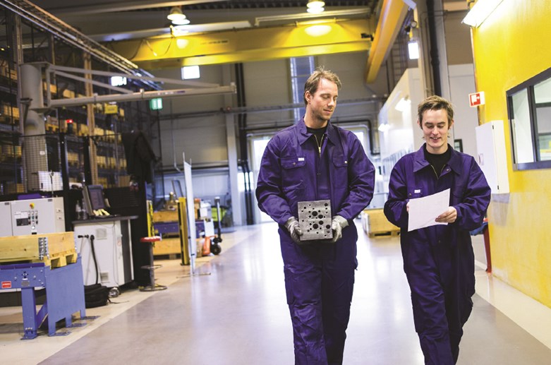 To ansatte går med blokk i handa på fabrikken i Kongsberg