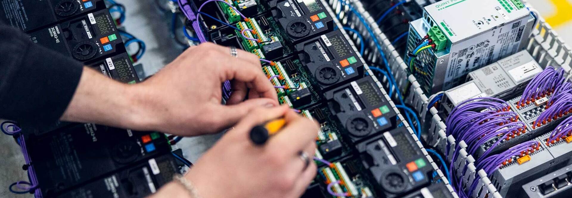 Et nærbilde av teknikerhender som kobler og monterer komponenter i et elektroskap | © Øyvind Welle