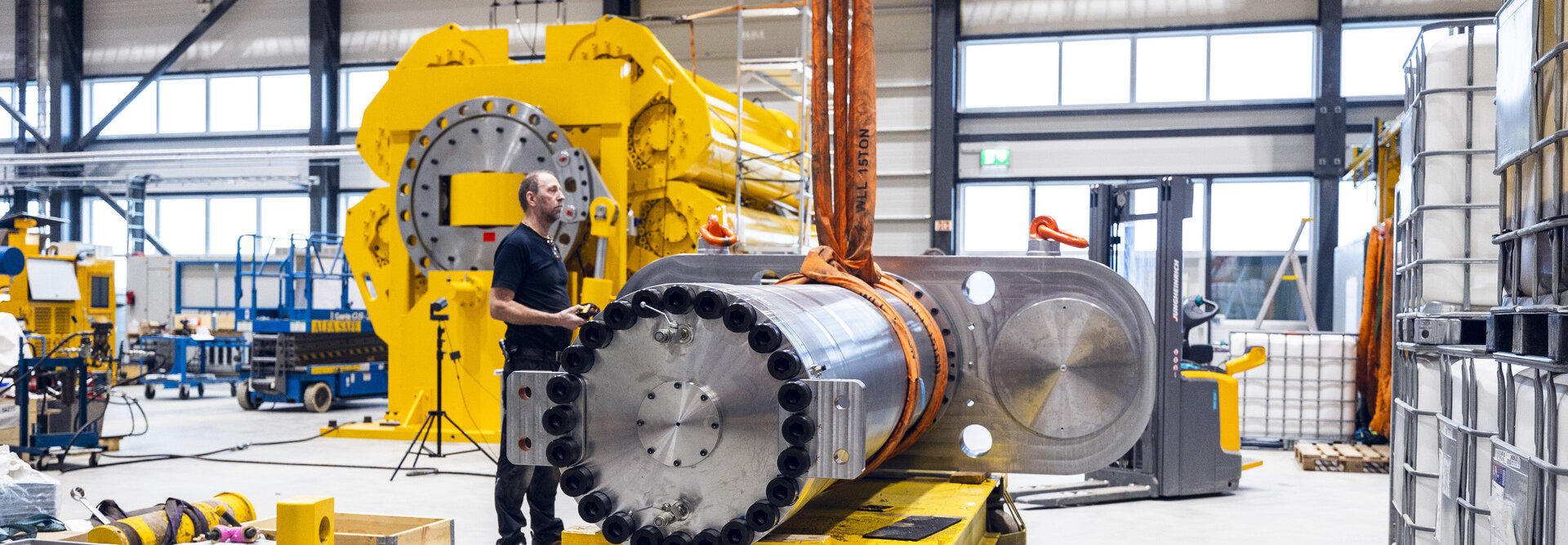 Production worker lifts 800T cylinder. Hydraulic damper 300T and pile driver in the background production hall Rissa