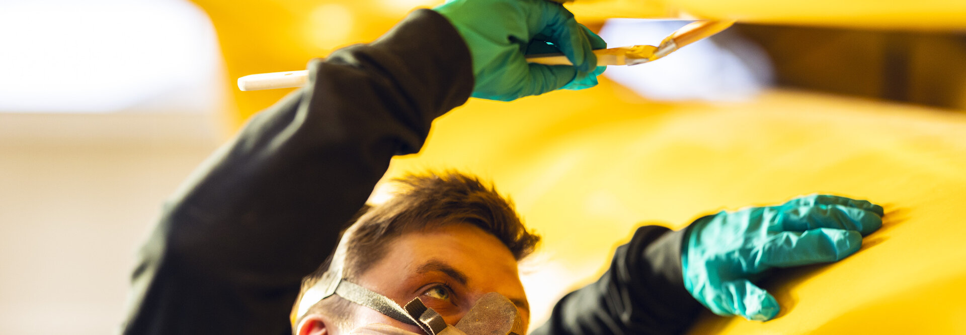 Person wearing mask while smearing yellow paint on a large hydraulic damper