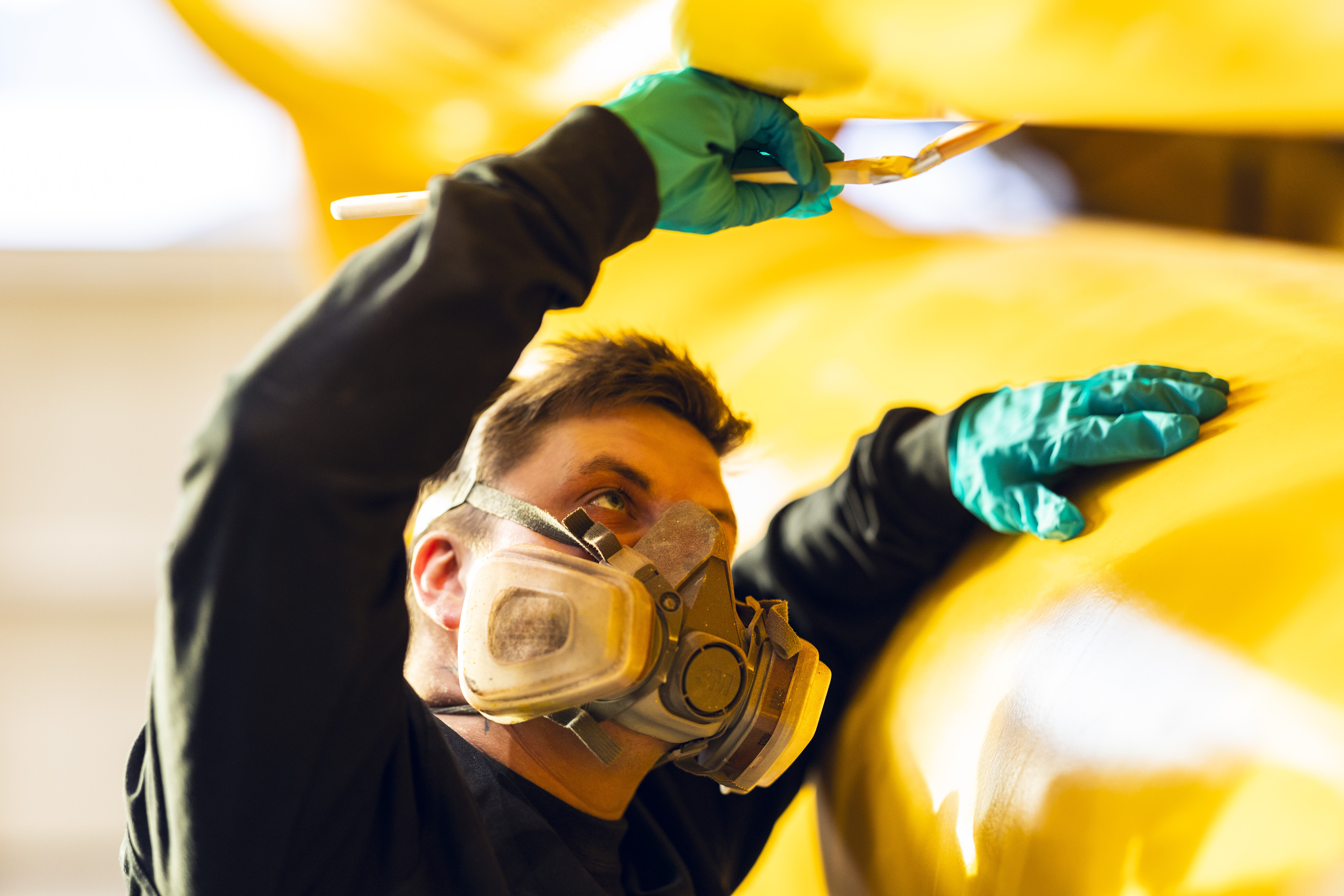 Person har på maske mens han flekker gul maling på en stor hydraulisk demper