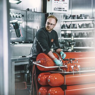 En person fikser akkumulator med flere hydrauliske komponenter i bakgrunnen